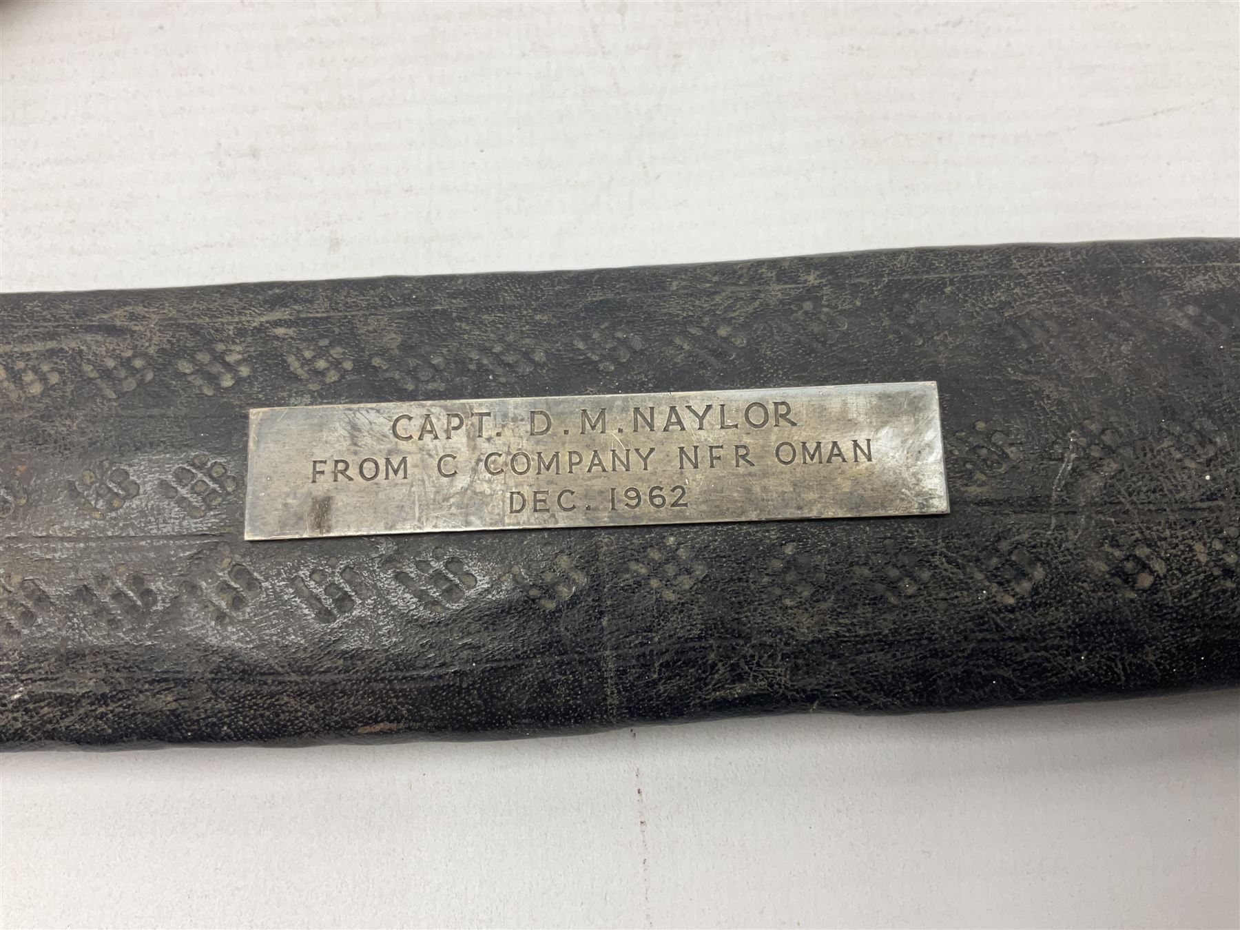 Omani presentation sword kattara, with 77cm  broad slightly curved single edge blade with two fullers, leather bound hilt woven with silver wire decoration and iron pommel;  in tooled leather scabbard with chased silver mounts and presentation plaque 'To Capt. D.M. Naylor From C Company NFR Oman Dec 1962' (Northern Frontier Regiment) L99cm overall