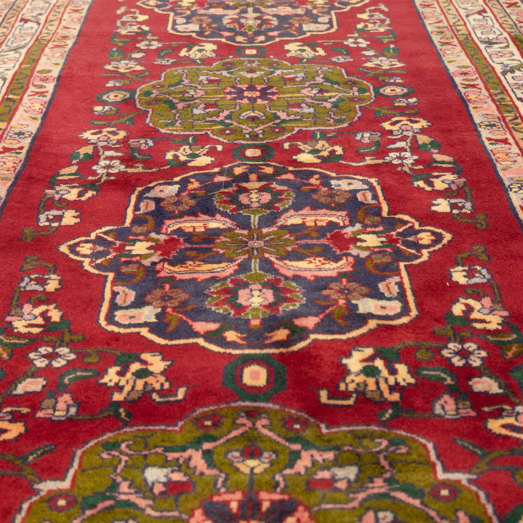 North West Persian Tariz hand-knotted runner, madder red field with a column of linked lozenge medallions in shades of indigo blue and pistachio green framed by stylized floral motifs within triple borders of rosettes and scrolling vines on an ivory ground, with cotton fringe ends