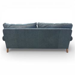 Late 20th century three seat sofa upholstered in green fabric, with gently rounded scroll arms, loose seat and back cushions, raised on turned wooden legs with castors, rear splayed legs