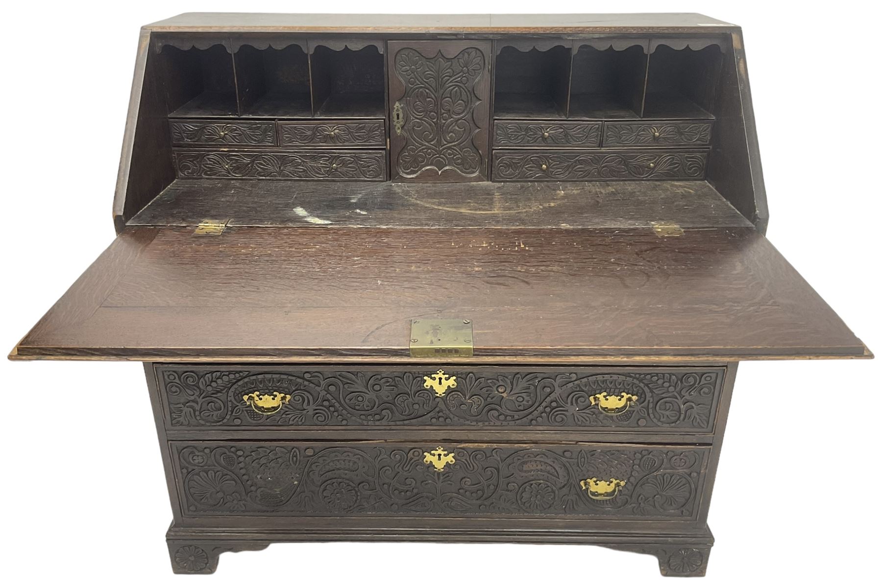 18th century heavily carved oak bureau, the fall front relief carved with three arches enclosing plants and flower head decoration, the interior fitted with pigeonholes, drawers and cupboard, four graduating cock-beaded drawers below, carved with lunettes and trailing foliage decoration, on bracket feet