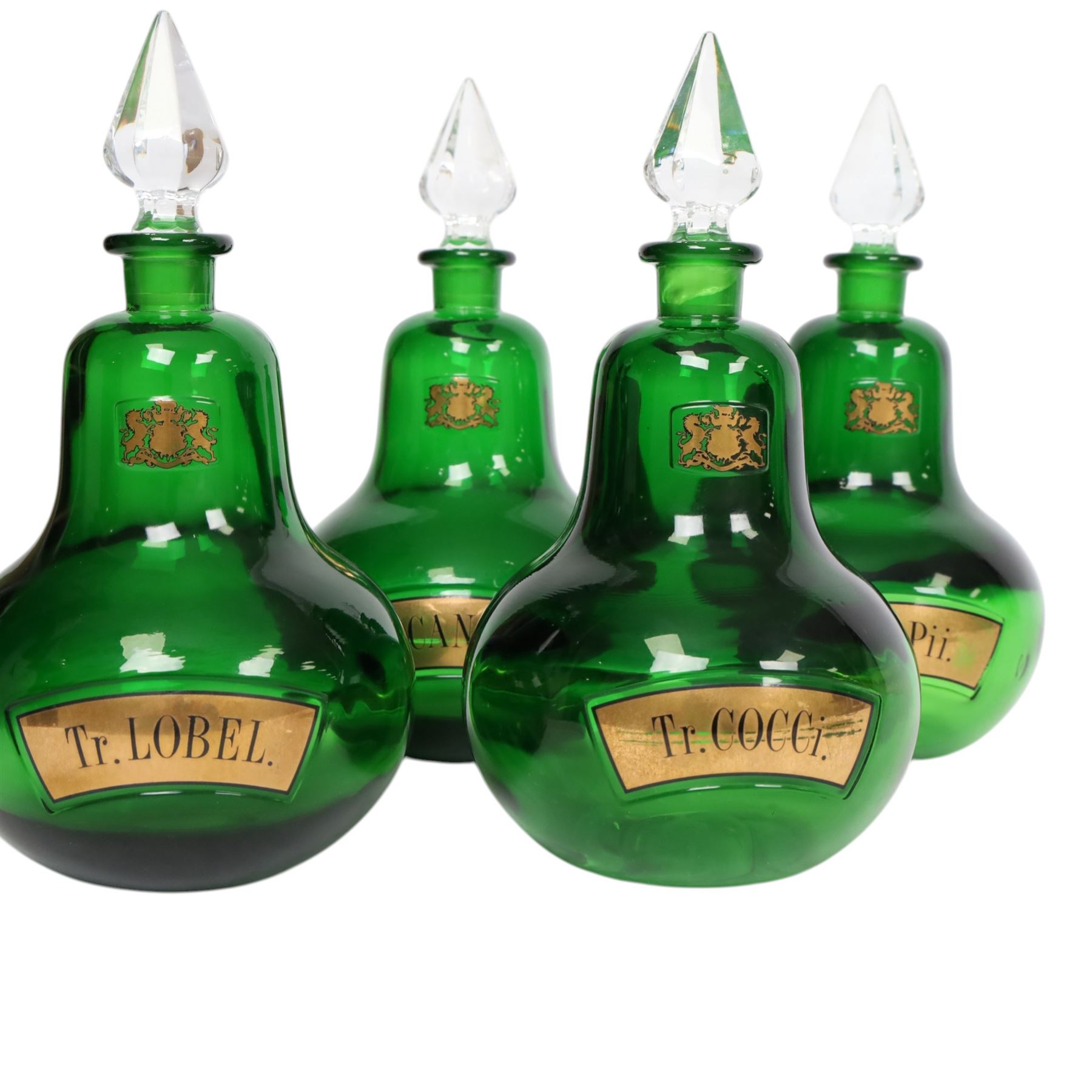 Set of four 20th century Royal Pharmaceutical Society green glass bottles, of bellied form with clear cut glass spire stopper, each body bearing gilt label in Latin: Tr.OPii., Tr.COCCi., Tr.CANNAB., and Tr.LOBEL., and gilt Royal Pharmaceutical Society crest to neck, H25cm

Provenance: From the collection of the family of Peter Green, a practising pharmacist whose career spanned the mid to late 20th century. During his professional life he managed pharmacies in Yeovil, Somerset, and later Selles Chemist in Filey, North Yorkshire, before purchasing and running his own business, Peter Green Pharmacy, located in the Market Place, Malton. The bottles were displayed as part of the traditional shop fittings in both the Filey and Malton pharmacies and were retained as part of his collection.