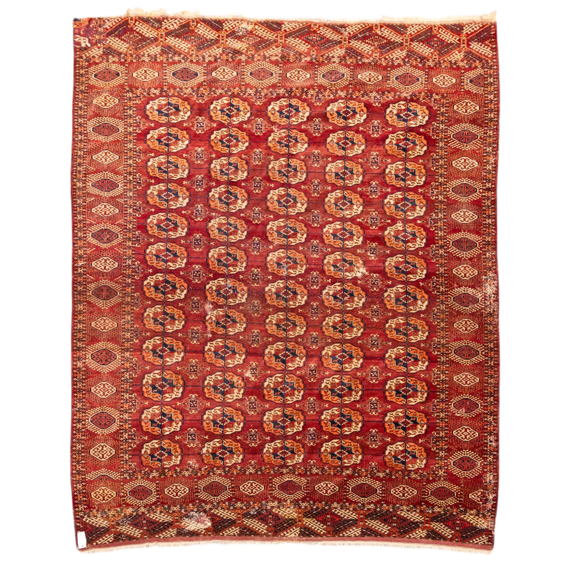 Vintage Bokhara hand-knotted rug, madder field woven in rows of octagonal Tekke guls arranged in vertical columns, each enclosing angular cruciform devices and tribal motifs, divided by narrow indigo lines, within multiple geometric borders incorporating stepped lozenges and latch hook devices, with cotton fringe ends 
