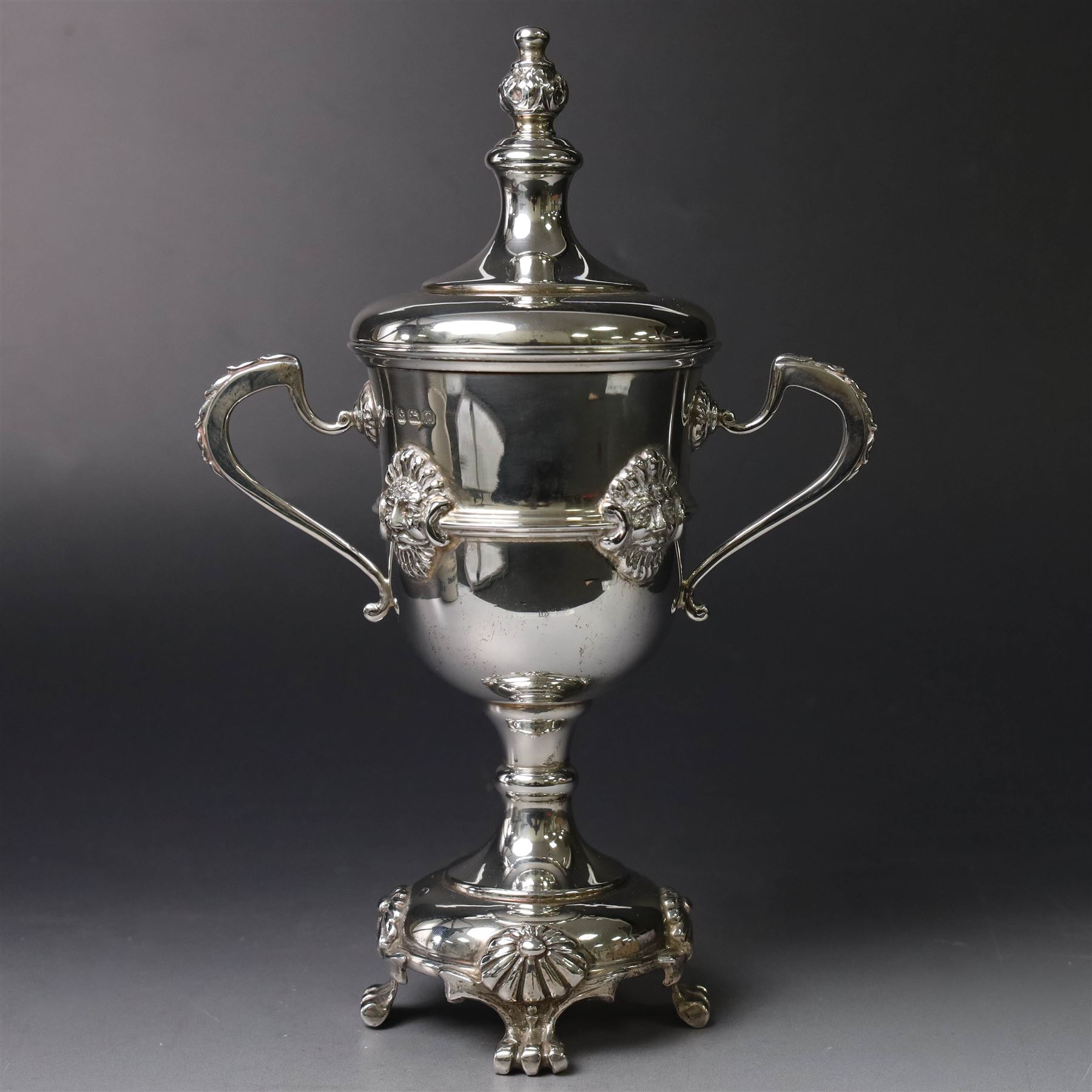 Mid 20th century silver twin handled trophy cup and cover, the bowl with central mask mounted girdle upon a knopped stem and spreading circular foot with flower head mounted paw feet, the tapering stepped cover with leaf moulded knop finial, hallmarked Vaughton & Sons, Birmingham 1938