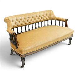 Late Victorian Aesthetic Movement settee, with buttoned upholstered roll-over back and arms, open spindle gallery frame with turned uprights, stuff-over seat, on shaped ebonised supports
