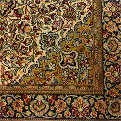 Fine Qom hand-knotted rug, ivory ground, with a dark navy shaped floral medallion and pendants, the field densely worked with fine flowering vines, palmettes and leafy scrolls in red, green, ochre and blue tones, within golden spandrels and a dark navy floral border, flanked by narrow guard stripes, with cotton fringes