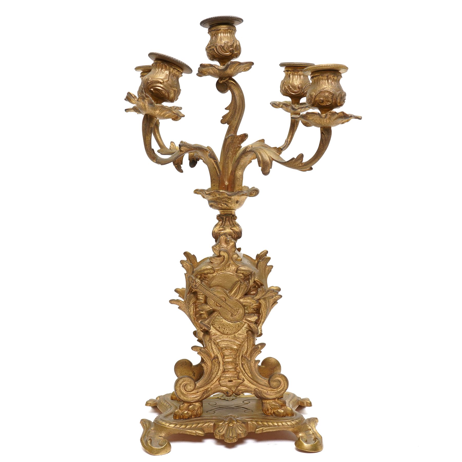 French-Late 19th century 8-day gilt brass rococo style mantel clock, c1890, waisted case  decorated with scroll work, leaves and musical instruments, resting on an attached plinth with splayed feet, dial within a glazed brass bezel with a gilt repoussé centre, porcelain cartouche Roman numerals and steel fleur-di-Lis hands, with a twin train movement, recoil anchor escapement and countwheel strike, sounding the hours and half-hours on a bell. With a matching pair of five-light candelabra. No Pendulum or Key.