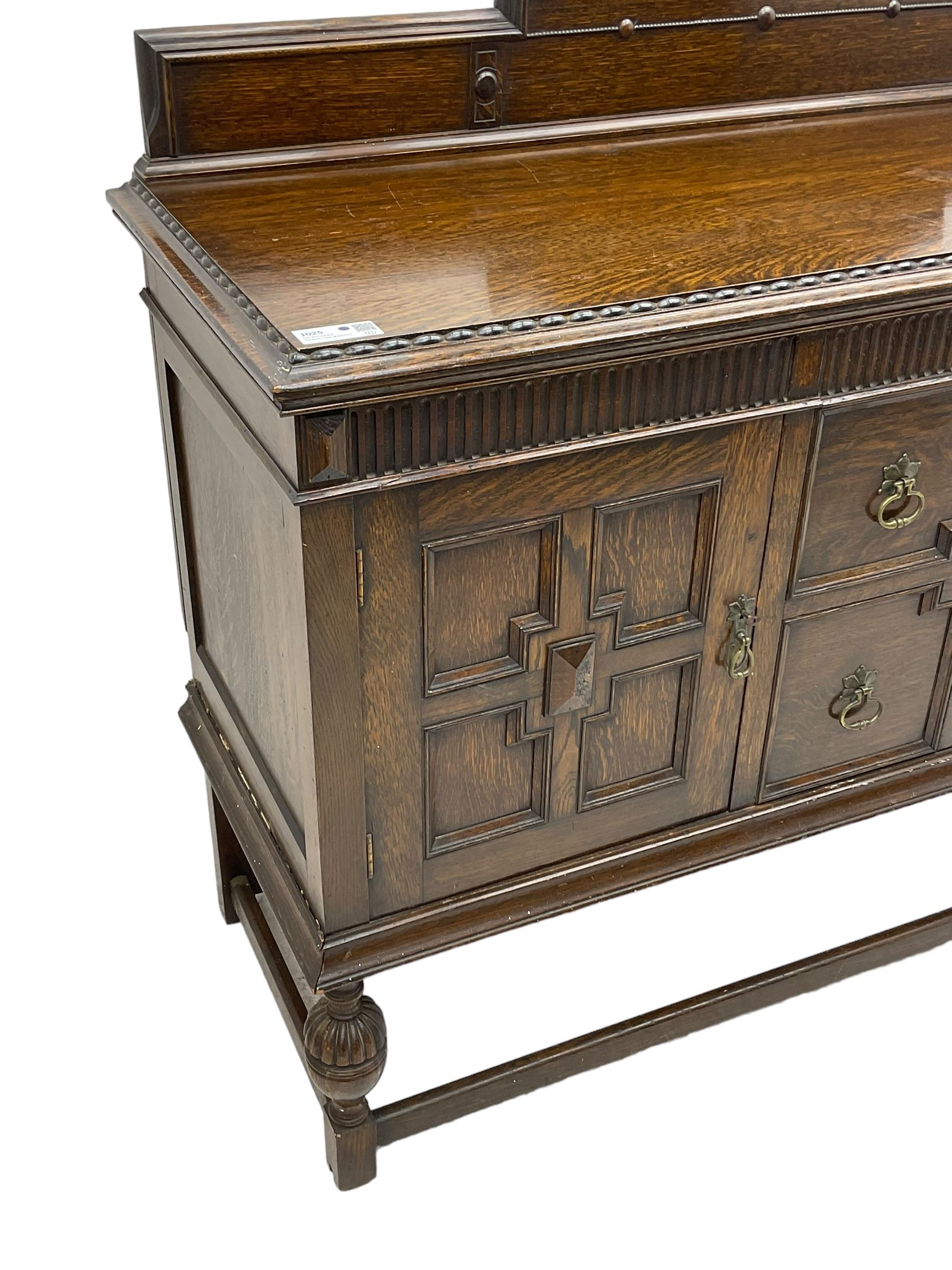 Early 20th century oak sideboard, raised stepped arch back over moulded rectangular top, fitted with two drawers and two panelled cupboards with geometric mouldings, on turned and lobe carved baluster feet united by stretchers 