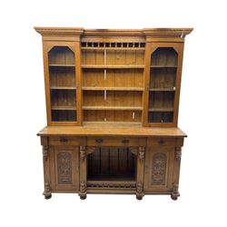 Late 19th century pine dresser, the projecting cornice with dentil and spindle moulded frieze above a three-tier plate shelves, flanked by glazed doors, the base fitted with three frieze drawers over arched apron and carved floral panelled cupboard doors, raised on turned feet