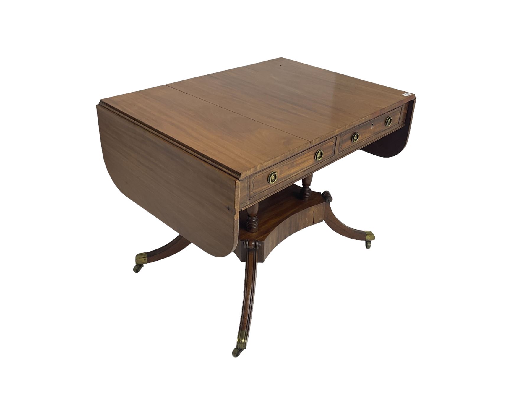 Regency period mahogany drop-leaf sofa table, rectangular top fitted with two cockbeaded drawers with ebony stringing, raised on turned columns united by quadrupod base, the sabre supports terminating in brass cups and castors