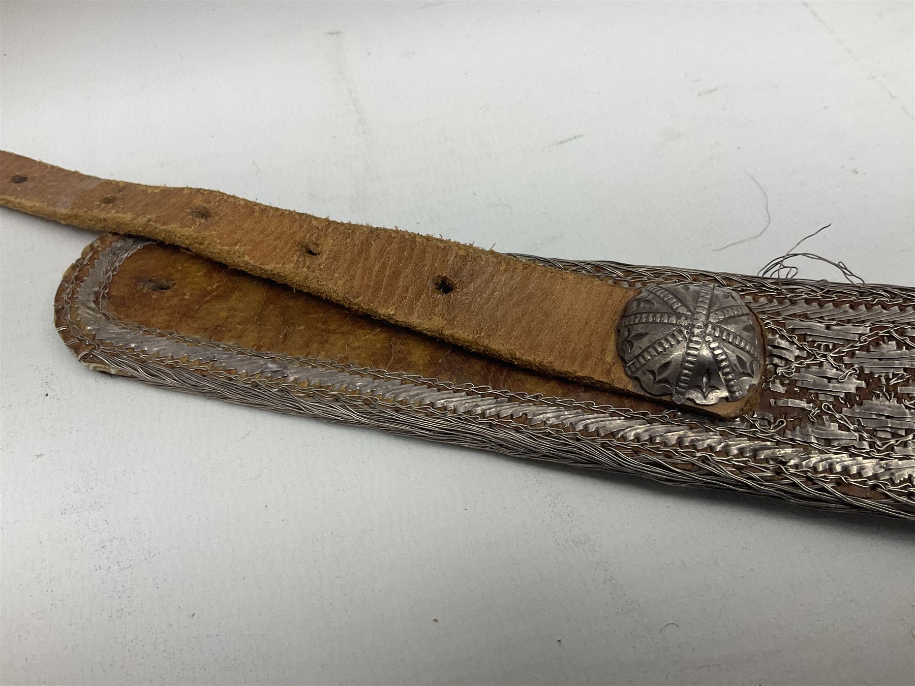 Omani Khanjar dagger, the 19cm curved blade with pronounced medial rib to either side, waisted hilt with dome shaped pommel and silver covered horn grip decorated with filigree bands, floral motifs and beadwork; in an intricately filigree decorated silver and leather scabbard with silver rings woven into the belt mount and fitted with original silver thread-work belt L34cm overall belt length 94cm