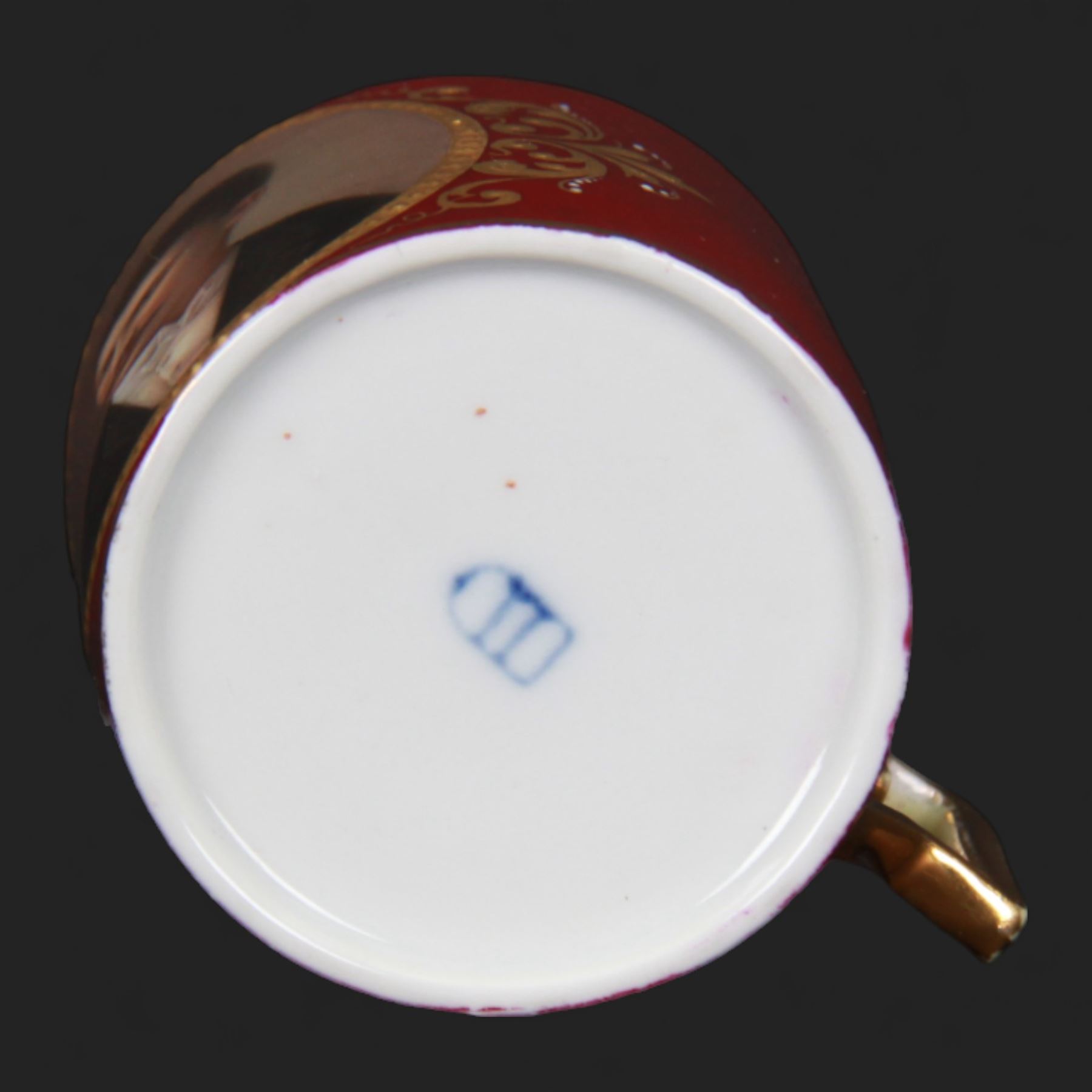 Late 19th century Vienna style coffee can and saucer, the cup with oval panel containing hand painted portrait of a gentleman, within a gilt foliate detailed surround, and upon a burgundy ground, the saucer with gilt band and sprigs upon a burgundy ground, with spurious shield mark beneath, cup H5cm saucer D12cm