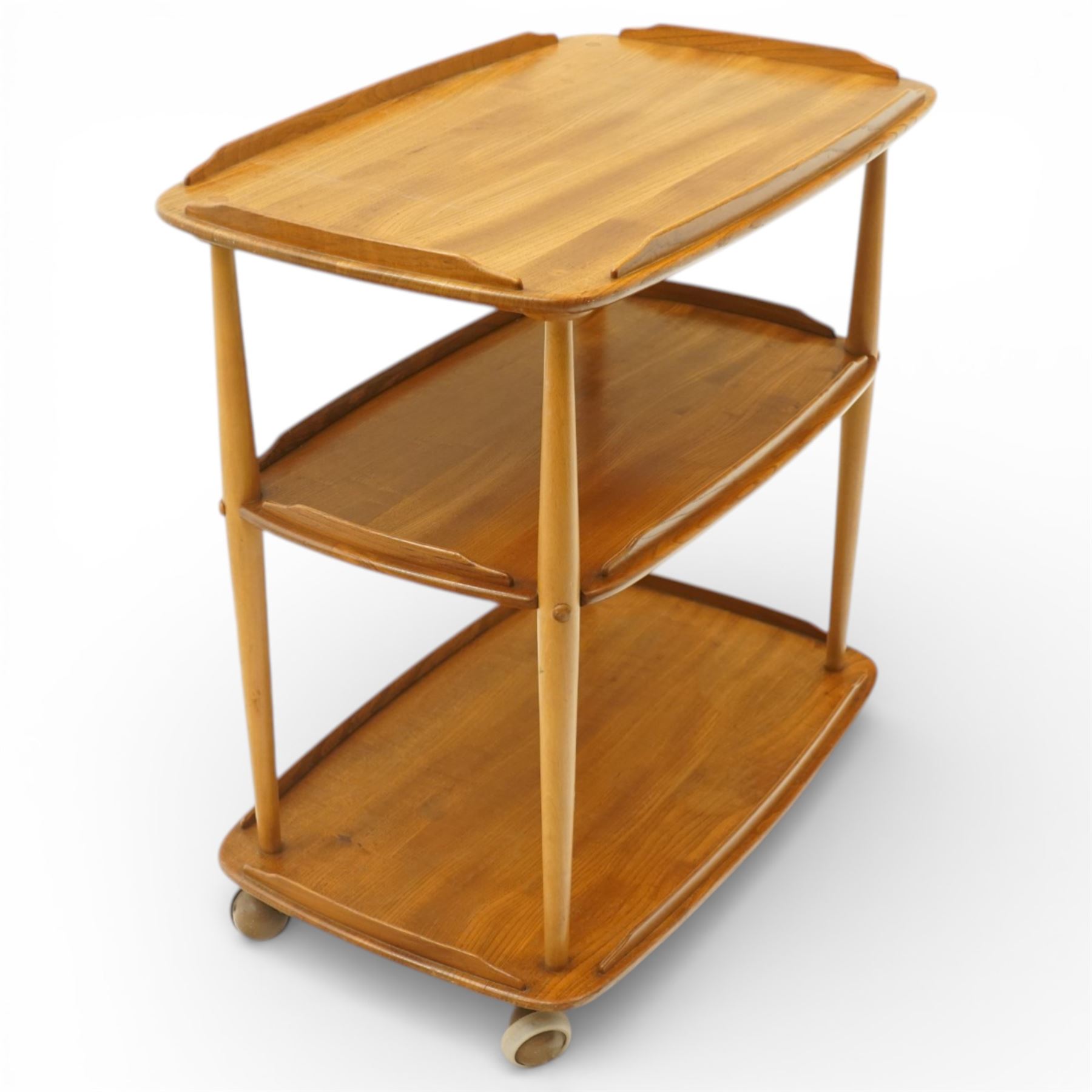 Ercol - elm tea trolley, Model 458. Rectangular three-tier form with shaped gallery edges, supported on turned upright supports, raised on castors