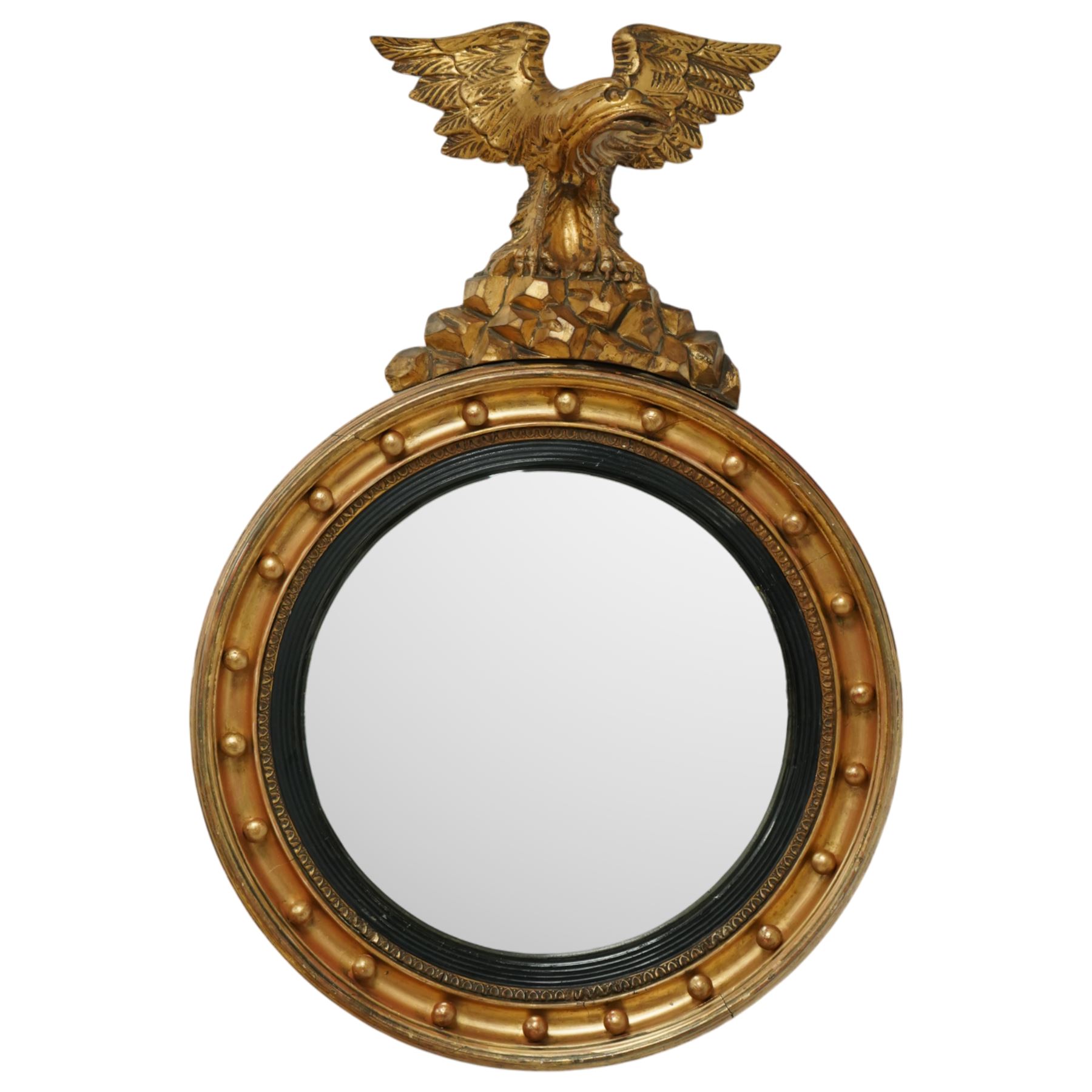 Regency period eagle mounted giltwood convex mirror, surmounted by a finely carved giltwood eagle standing on rocks above the circular mirror with the original mirror plate and surrounded by a fluted ebonized slip and the convex frame with gilt ball decorations, the back with label for ‘T.G. Woof Ltd, manufacturing cabinet makers, Devonshire Street, Sheffield