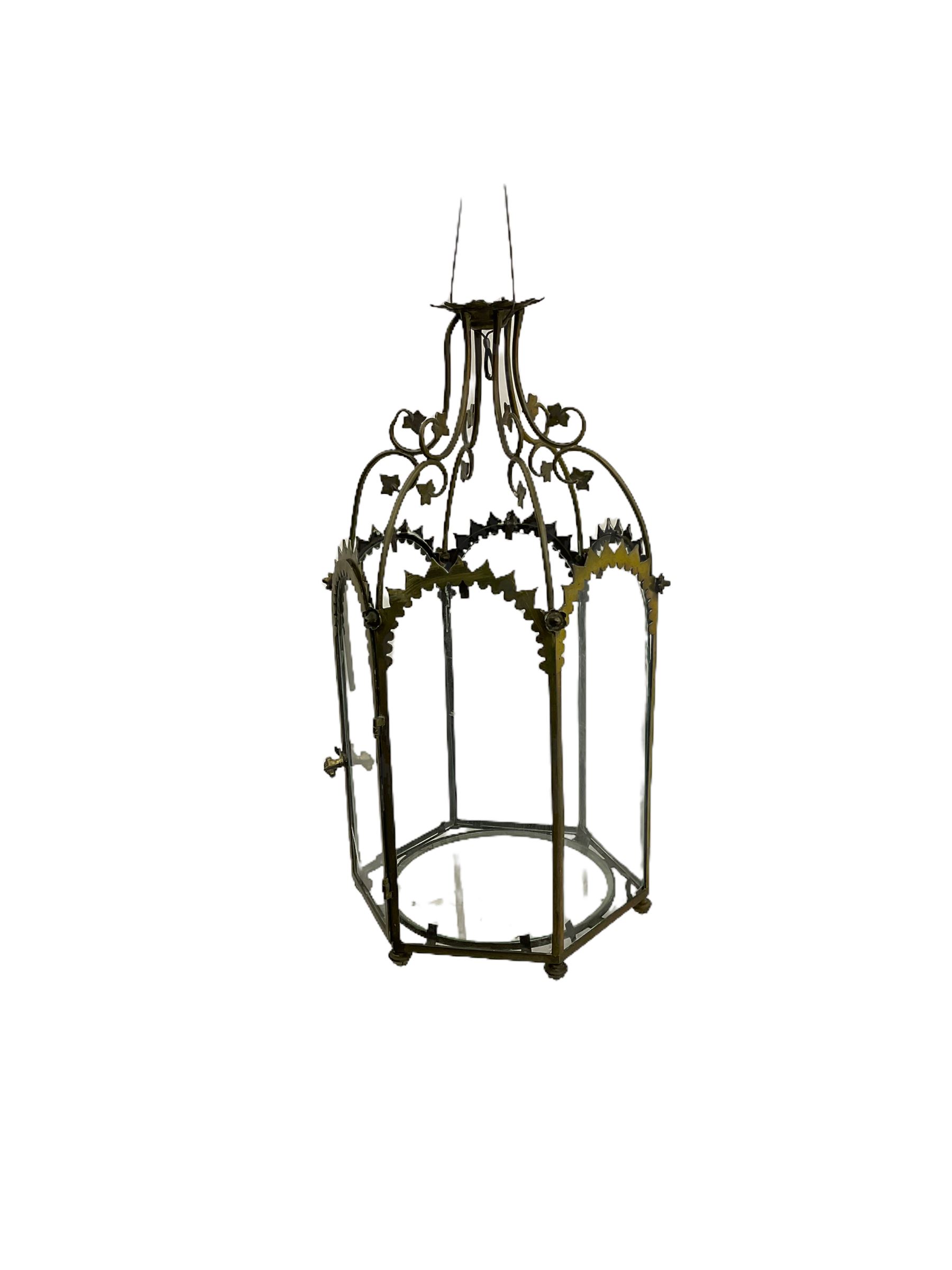 19th century brass and clear glass hexagonal hall lantern, with scrolling wire work open domed top over six arched panels, including a hinged door, the base enclosed with a circular glass panel on turned feet, H64cm