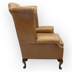 Contemporary set of two tan leather armchairs, comprising a deep-buttoned chesterfield and a matching wingback chair, both with rolled arms, studded borders