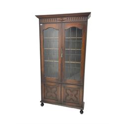 Early 20th century oak bookcase on cupboard, arcade carved frieze over astragal glazed doors enclosing three adjustable shelves, over cupboard base, on bun feet