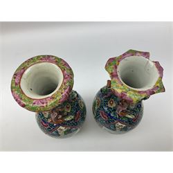 Pair of 19th Century Clobbered Chinese Export vases, with lobed rim and applied twin temple lions and dragons to the waisted neck, decorated with enamel panels of traditional scenes of figures and buildings, surrounded by blossoming flowers, H20cm