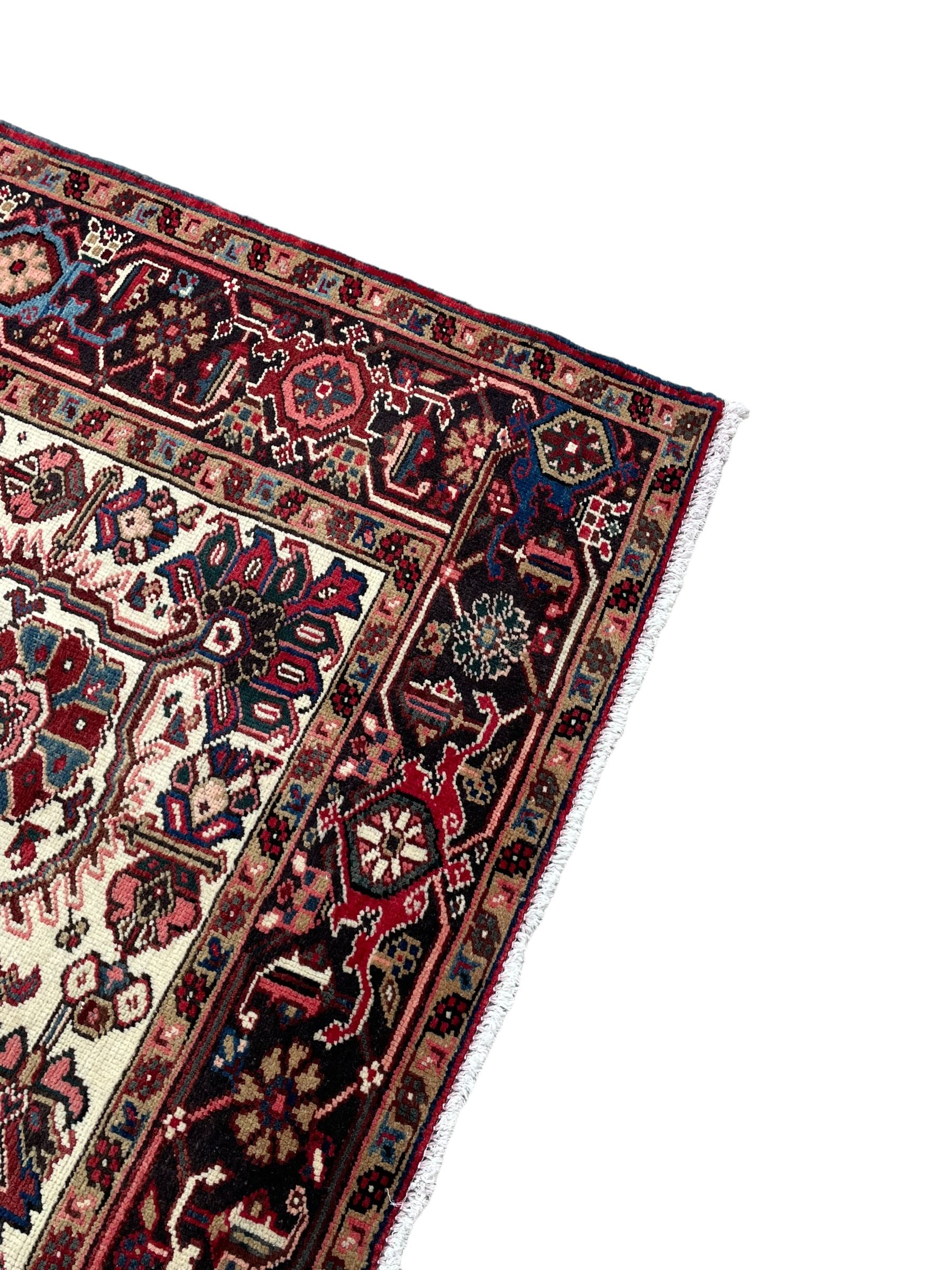Persian Heriz red ground rug, central scrolled medallion on dark ground decorated with floral motifs, the surrounding field decorated with stylised plant motifs and smaller geometric symbols, guarded border with repeating pattern punctuated with rosettes and flower heads 