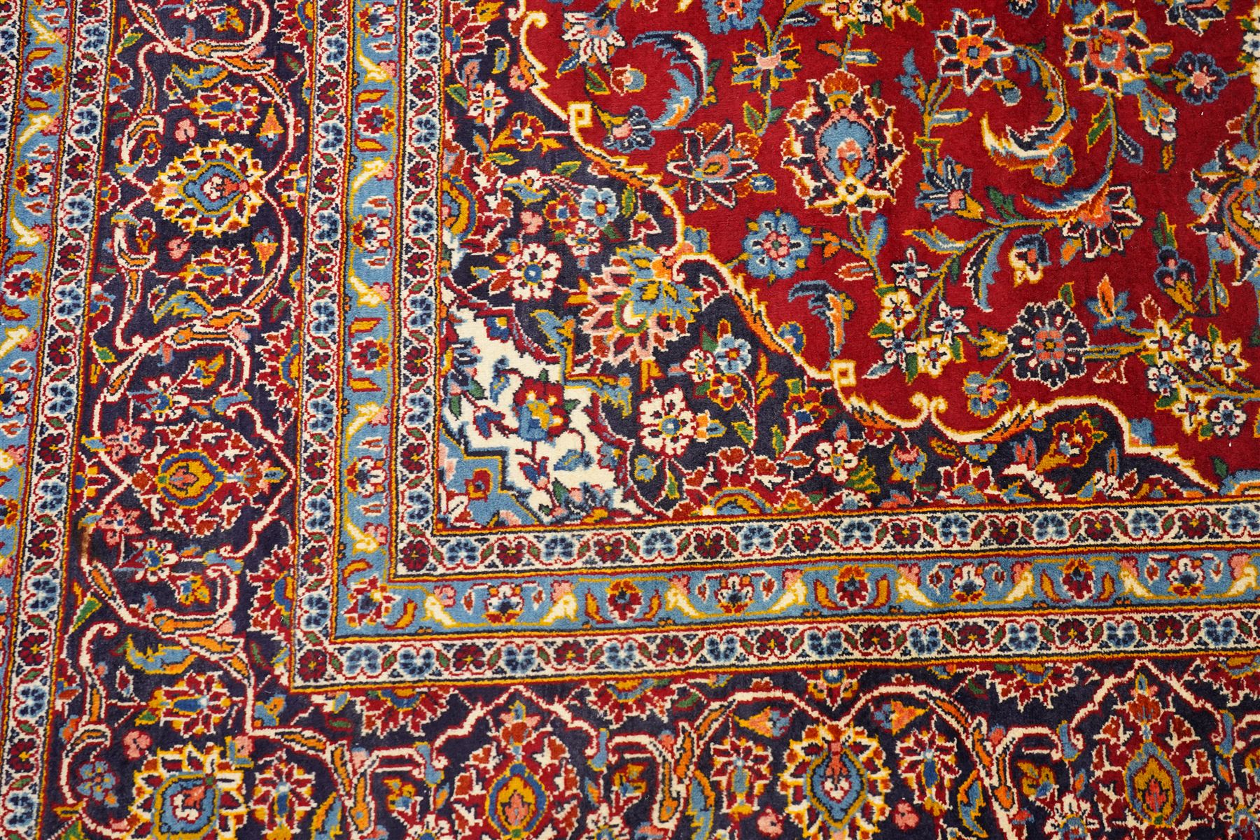 Central Persian Kashan hand-knotted carpet, crimson field with central cusped medallion in ivory, pale blue and indigo, issuing a network of scrolling arabesques, palmettes, and floral sprays, with conforming spandrels, main border of scrolling vinery and stylized palmettes, framed by multiple guard borders, with cotton fringe ends 
