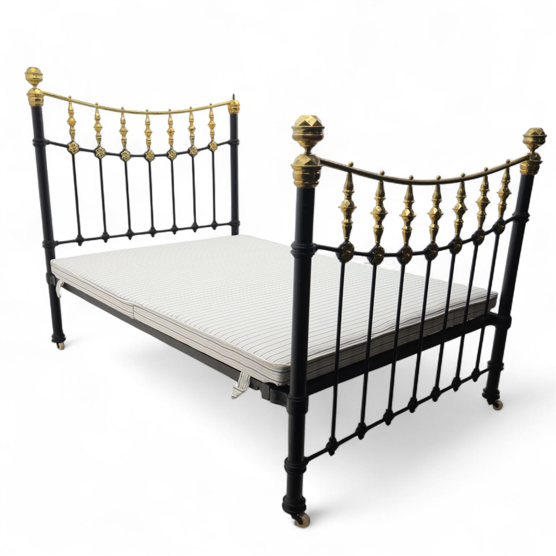 Victorian brass and iron 4' 6'' double bedstead, curved brass top rail with cast iron spindles and ornate floral rosettes flanked by urn shaped finials, foldable divan style base upholstered in a striped fabric, supported on turned posts and ceramic castors