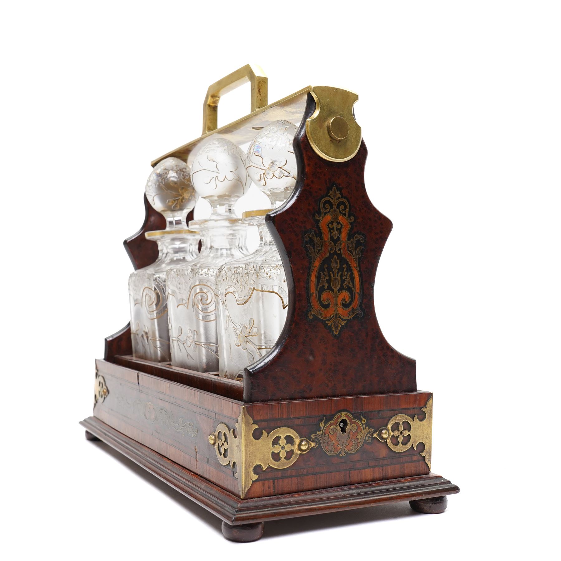 Amboyna three bottle tantalus, the cut glass spirit decanters decorated with raised naturalistic decoration heightened in gilt, with brass corner mounts and singular carrying handle, H32cm