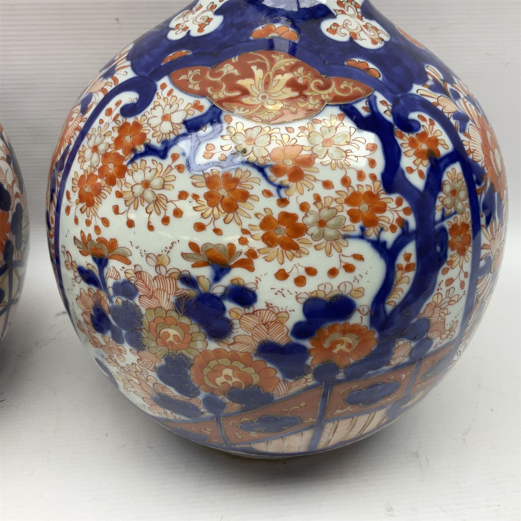 Pair of large 19th century Japanese Imari porcelain bottle vases, painted with shaped reserves of peonies, chrysanthemums and prunus blossom, each H46cm