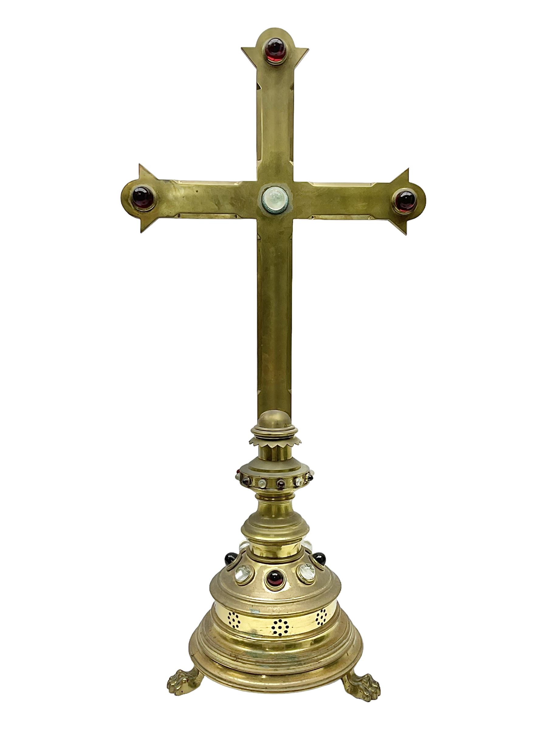 Brass alter cross, decorated with glass cabochons, upon a acicular stepped base and three claw feet, H73cm 