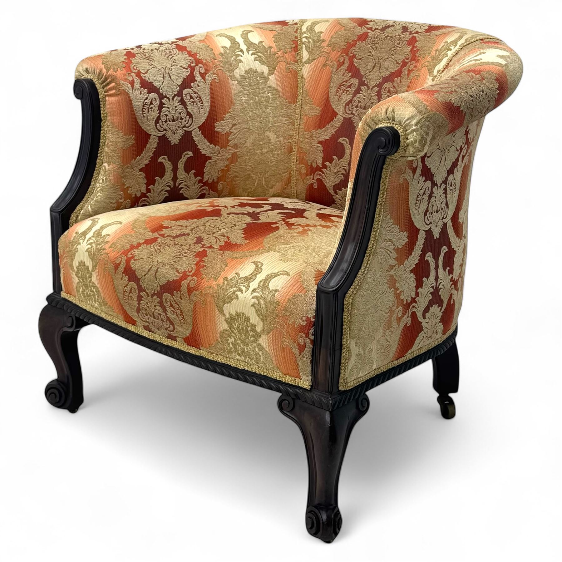 Early 20th century mahogany framed upholstered tub armchair, scrolled arms, upholstered in a damask-style fabric with foliate pattern, raised on cabriole front legs upon brass castors