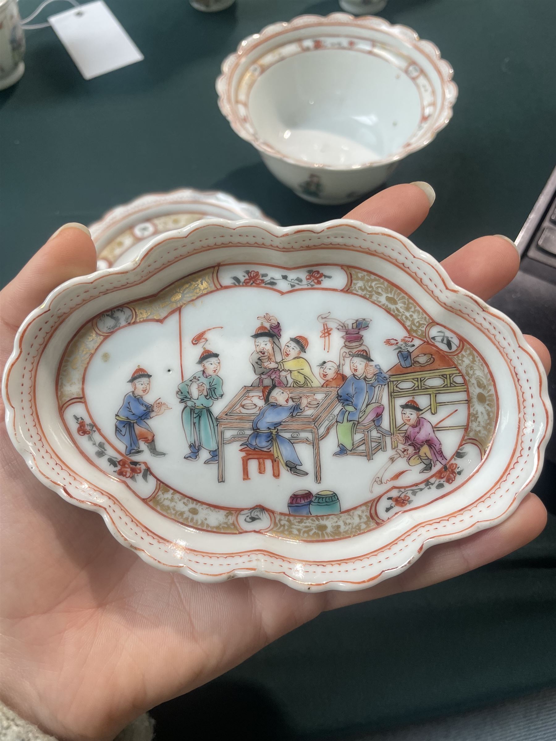 Set of Chinese 20th century tea wares, comprising three bowls of graduating sizes, teacup, spoon rest and small plate, decorated with scenes of figures around a table, each with scalloped rim, largest bowl D12cm