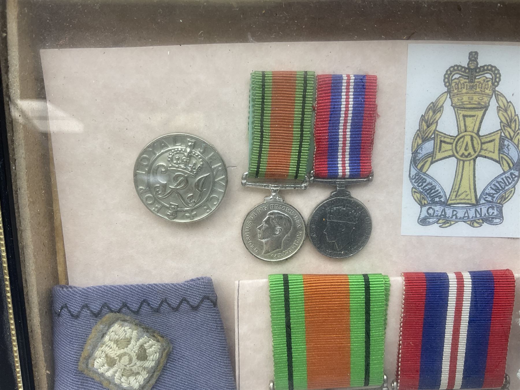 Framed display of medals and badges relating to Captain Cynthia Page of Queen Alexandra's Royal Army Nursing Corps including WW2 War Medal and Defence Medal with miniatures; Red Cross Society 3-Year Service Medal; Q.A.R.A.N.C. cap badge; Girl Guide and silver Scout badges; rank epaulettes; and related photographs 33 x 23cm