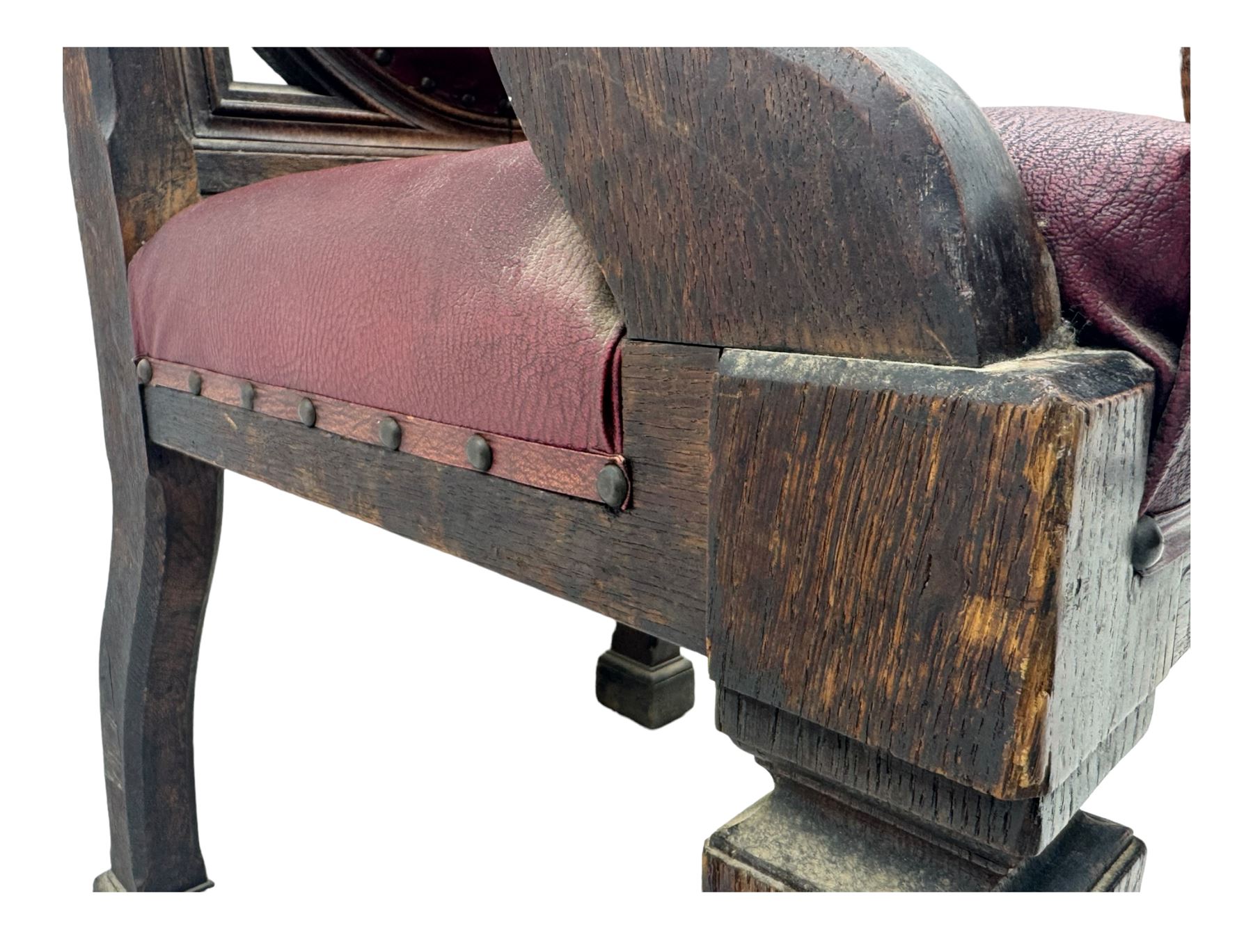 Late Victorian Gothic-revival armchair, arched crest rail carved with tracery and trefoil detail, padded circular back and seat, brass studded burgundy leather upholstery, shaped armrests with scrolled terminals, on square tapering supports