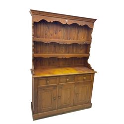 Pine dresser, raised back with projecting cornice and shaped apron over two tier plate rack, base fitted with three drawers and three panelled cupboard doors, on plinth base