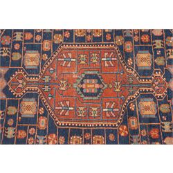 Persian Heriz hand-knotted carpet, terracotta ground centred by large dark navy geometric medallion with stepped outline, decorated throughout with stylised flowerheads, palmettes and geometric motifs in blue, green and ochre, enclosed by diagonal geometric border with narrow guard stripes