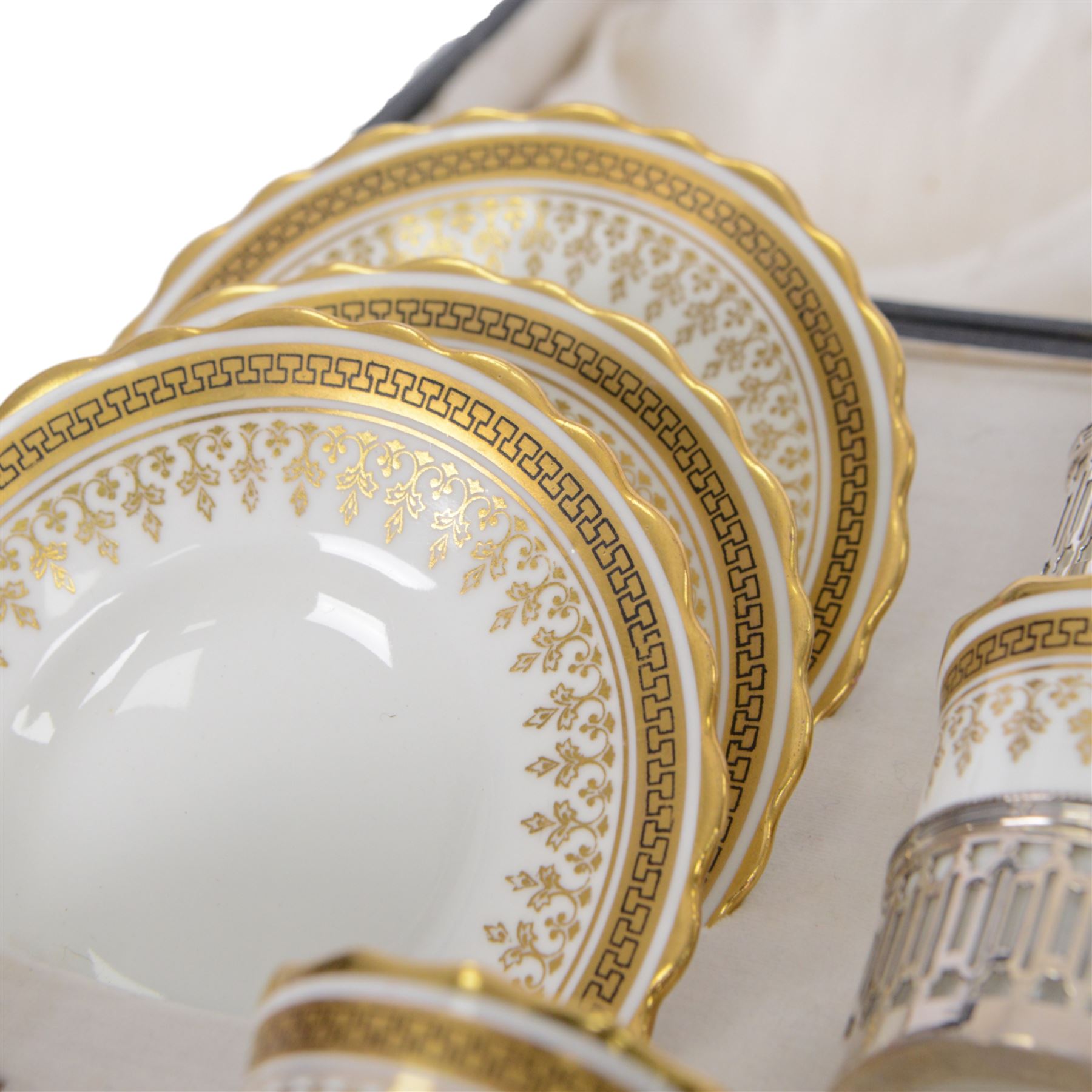 Boxed set of six Aynsley coffee cans and saucers, decorated with gilt greek key border, the cans within silver mounts, hallmarked Birmingham 1911