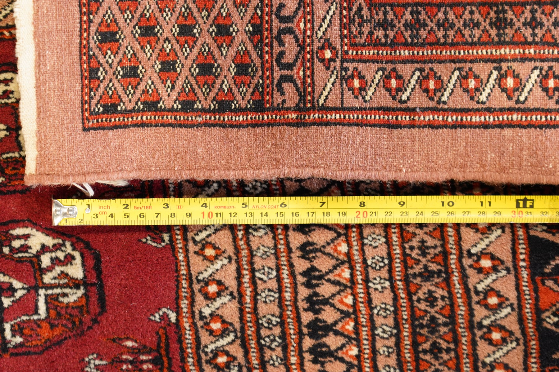 Large Afghan Bokhara crimson ground carpet, the field with rows of repeating Gul motifs and geometric design, enclosed by multiple repeating geometric guard bands