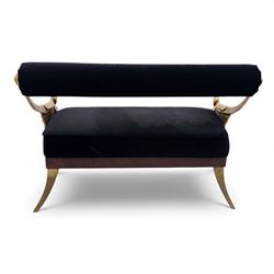 Late 20th century pair of Empire inspired brass metal framed two-seater sofas, upholstered in black velvet with cylindrical backrest and sphinx form arms terminating in paw feet, together with matching deep buttoned black velvet footstool on brass capped legs (Footstool H 38cm, W 70cm, D 70cm)