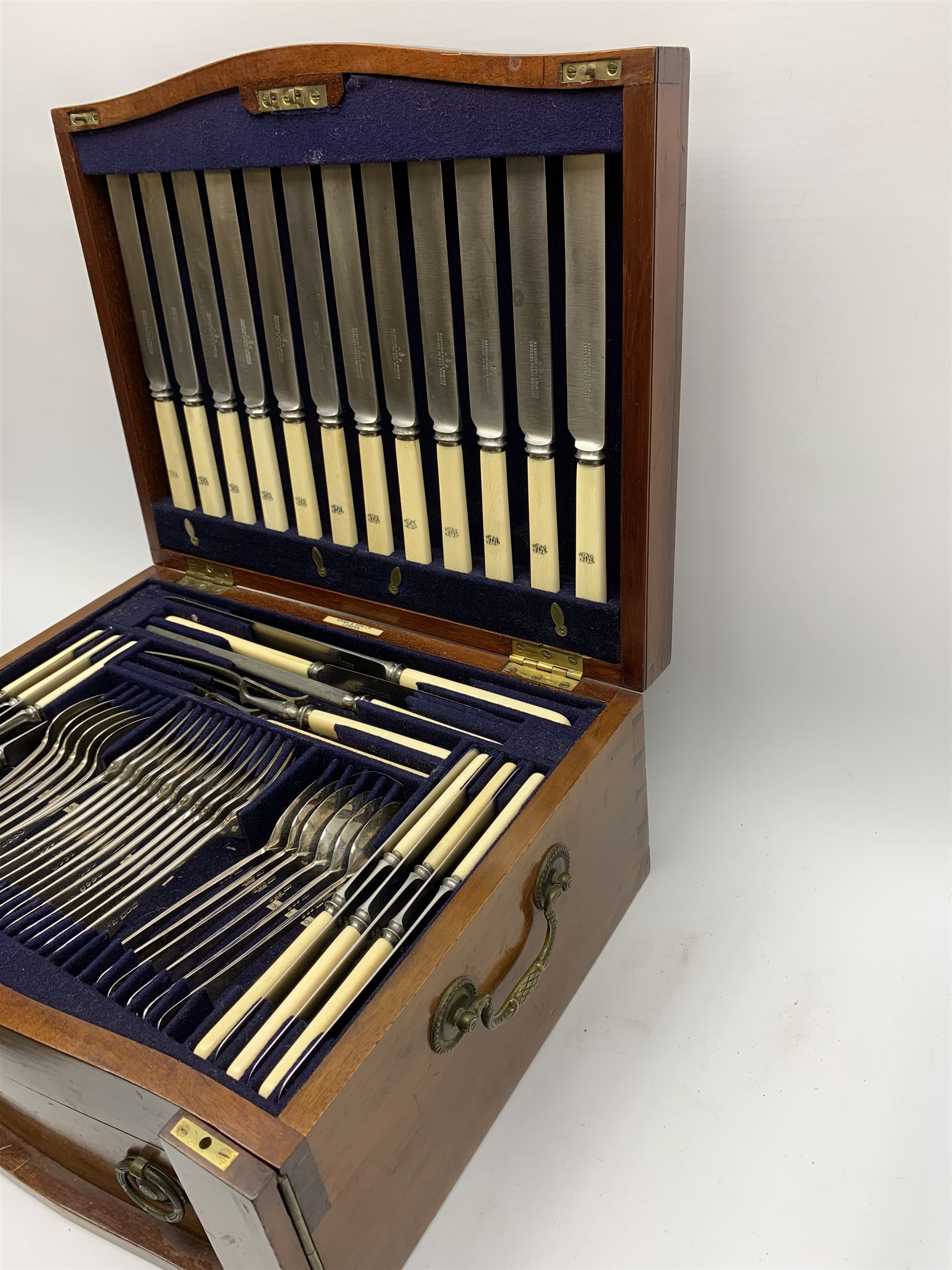 Late 19th/early 20th century composite canteen of silver flatware, contained within an early 20th century mahogany serpentine fronted case with twin drop carry handles, and hinged cover with boxwood stringing and central inlaid shell motif, above a single drawer with twin ring handles and Wellington style locking system, the cover and drawer opening to reveal plaque for Spink & Sons Ltd London, and fitted interior containing ivory handled knives, ivory handled carving set, and silver Hanoverian and Old English pattern cutlery, each with engraved monogram to terminal, hallmarked London, makers Spink & Son (John Marshall Spink), Goldsmiths & Silversmiths Co, and Chawner & Co (George William Adams), various dates ranging 1880-1923, gross weighable silver 92.59 ozt (2880 grams)