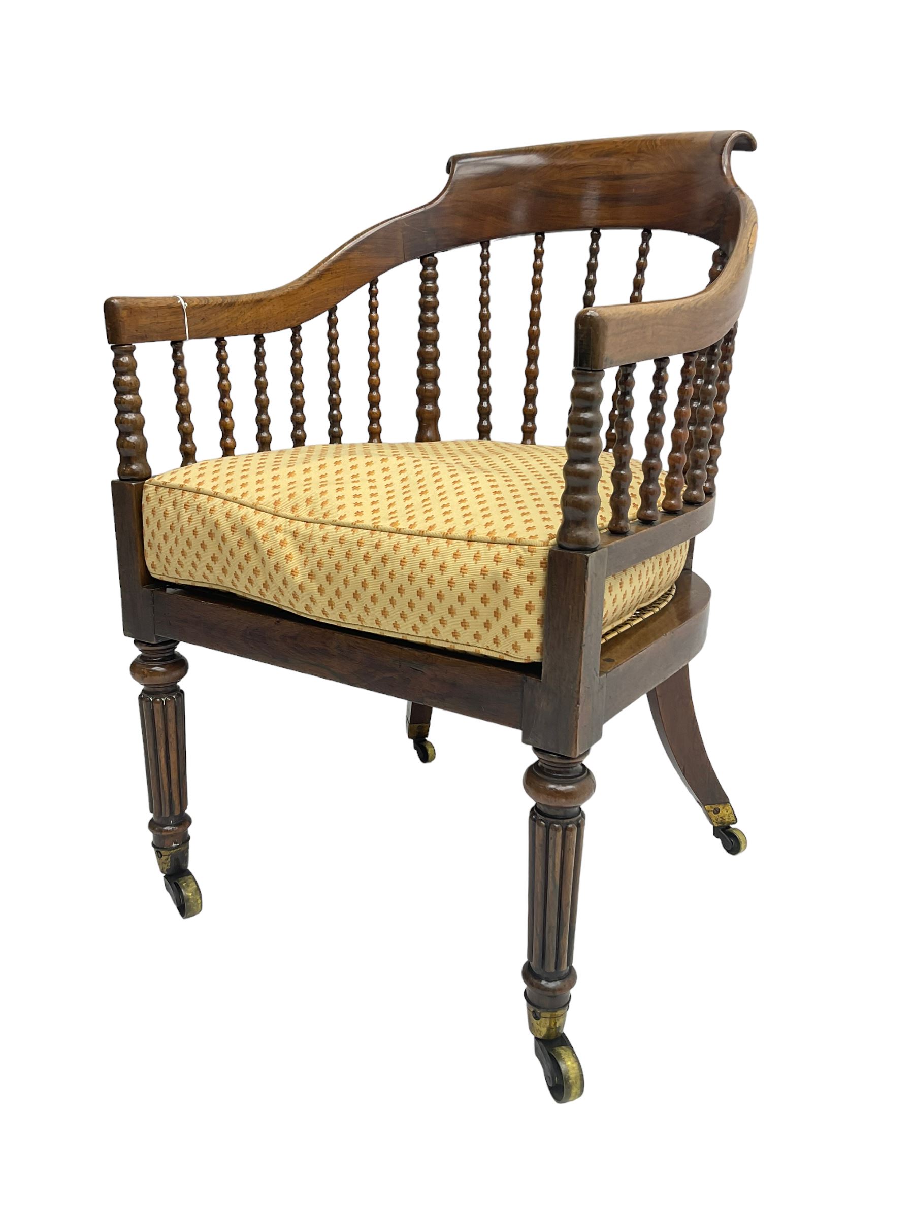 William IV rosewood tub armchair, the arched bow cresting rail over graduated bobbin turned spindles, cane seat with loose cushion, terminating in brass cups and castors.