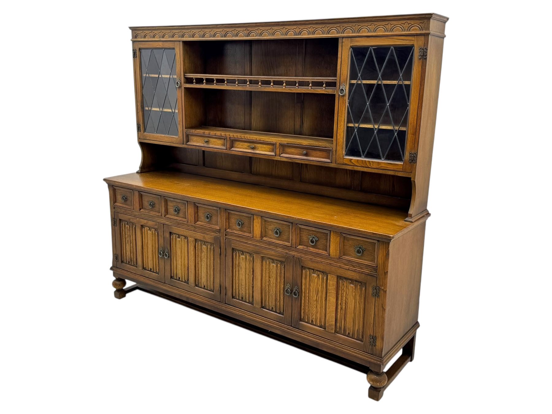 Large mid-20th-century oak dresser with two astragal glazed doors between gallery shelf and lower shelf, with three short drawers and lower section with four drawers and three double-panelled linen-fold hinged cupboard doors 
