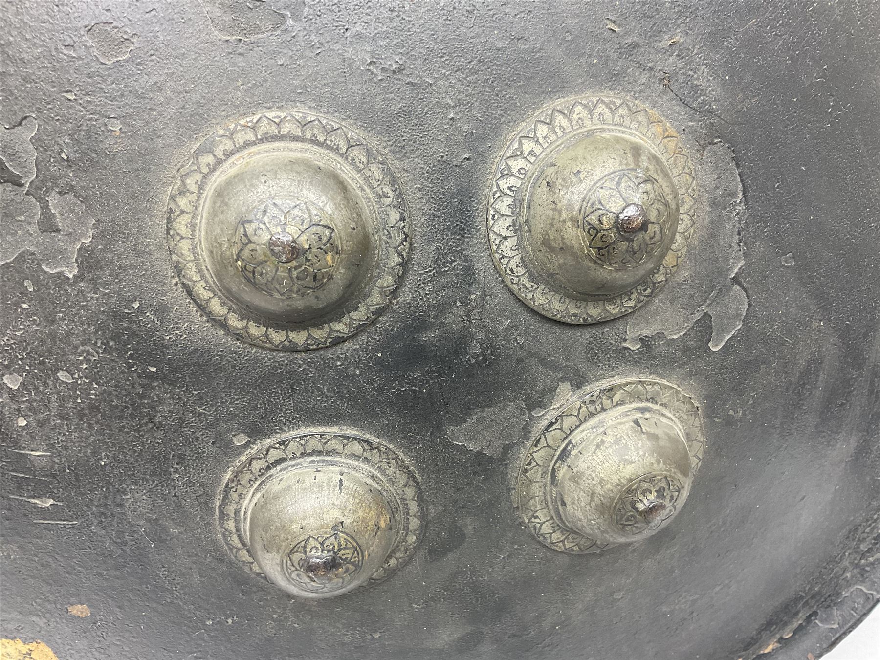 Indian black lacquered hide shield/dhal, of circular convex form with strongly outward-turned brim, fitted at its centre with four metal bosses, each of hemispherical form, with traces of silvered foliate decoration, the bosses corresponding on the inside with four iron rings for enarmes D49cm