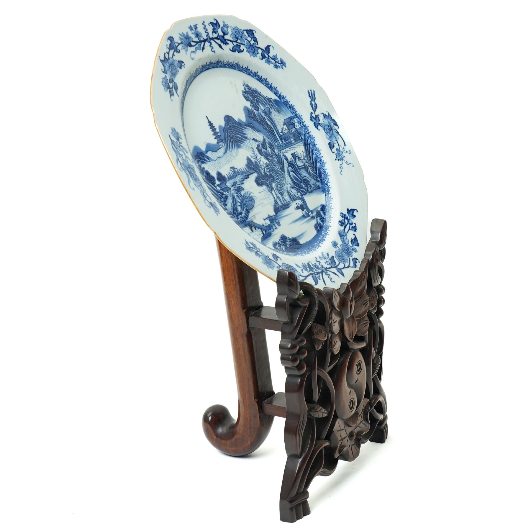 18th century Chinese plate of octagonal design decorated in blue and white with figures by a river with buildings etc W30cm on a 19th century hardwood stand