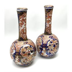 Pair of late 19th century Japanese Imari porcelain bottle vases with covers, painted with shaped reserves of peonies, chrysanthemums and prunus blossom, against a foliate and diaper ground, heightened with gilt throughout, each with character mark beneath, H32cm