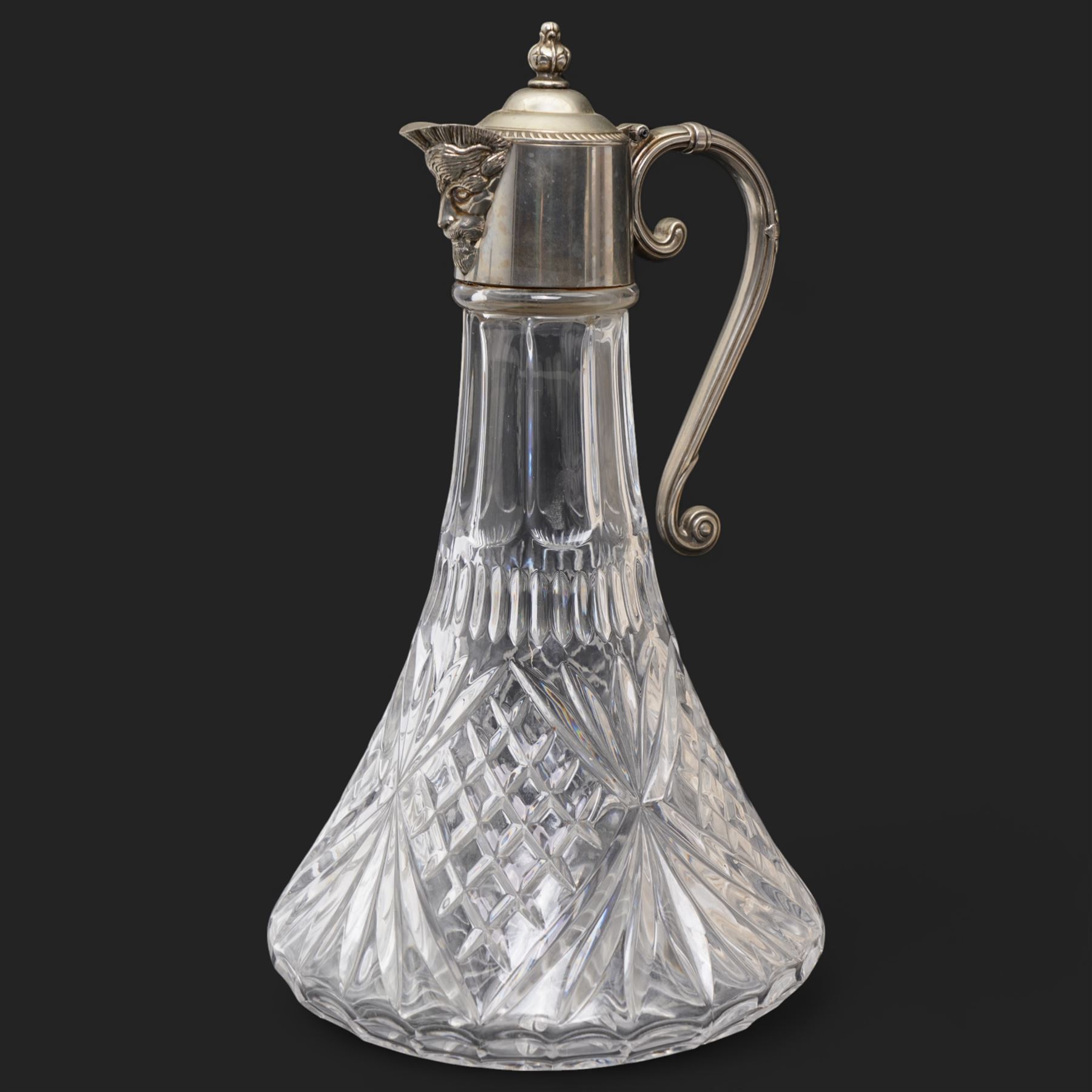 Composite plaque, depicting Sprites in a garden, with inset 'Arts and Commerce Promoted' medallion to reverse, 20cm x 33cm; together with a moulded glass Claret jug with silver plated mount H30cm 