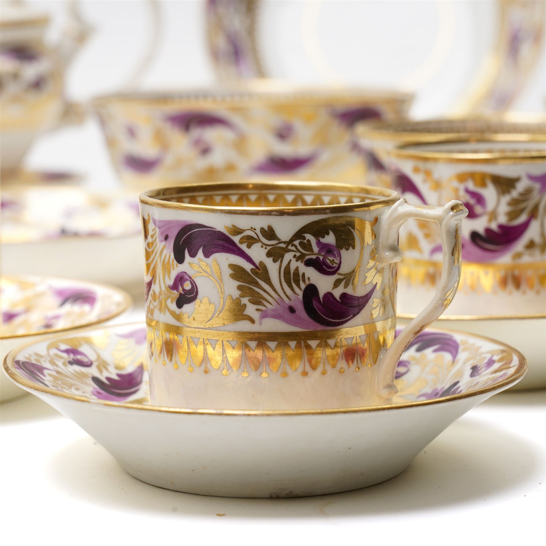 Early 19th century Derby tea and coffee service painted with a border pattern of purple and gilt leaves and flowers comprising four large cups with five saucers, nine coffee cans with twelve saucers, tea pot and stand, slop bowl, milk jug and two plates, red painted mark.