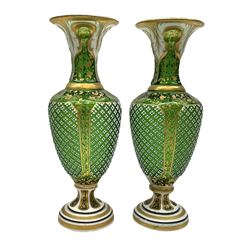 Pair of Bohemian green glass vases, overlaid in white with leaf panels and gilded detail, upon overlaid spreading feet, H22cm