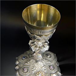 20th Century silver plated Gothic chalice, embossed throughout with fleurs de lis, foliate and bead decoration, on a knopped stem with flared and cusped foot, inset with three amethyst and two blue paste stones and applied paste and split pearl brooch, engraved beneath 'In Memory of my Mother R.I.P ... Aug 15th 1937, H23cm