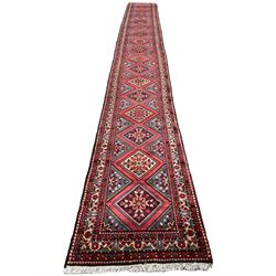 Persian Hamadan runner, red ground, decorated with eighteen lozenge medallions decorated with stylised floral motifs, three band border decorated with plant motifs and geometric patterns
