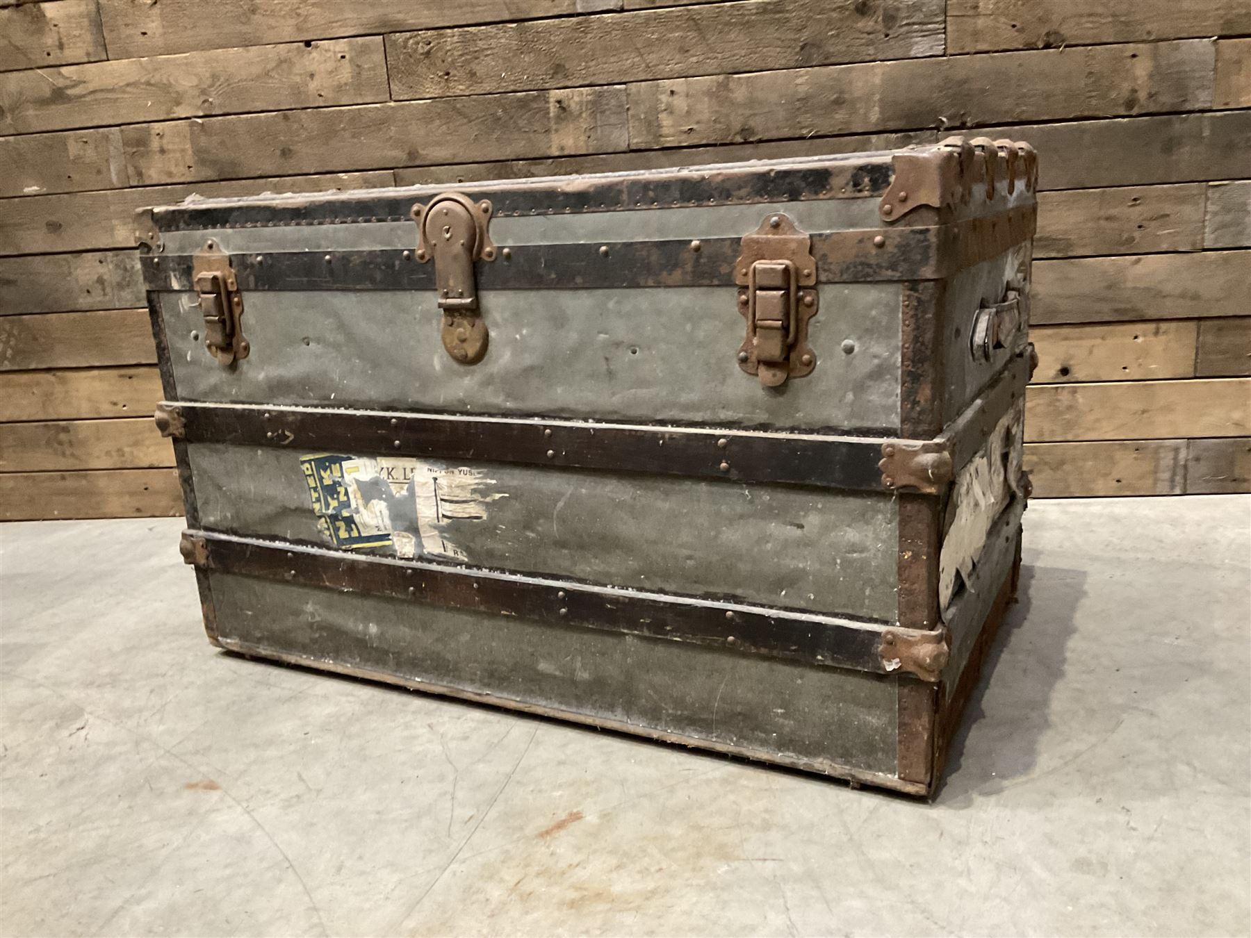Early 20th century wood and metal bound zinc travelling trunk, hinged top with three clasps, decorated with period luggage labels