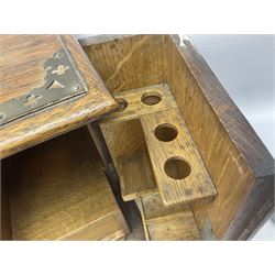 Early 20th century oak smokers cabinet, with brass shield shaped mounts, opening to reveal a compartmentalised interior with three drawers, pipe rack and tobacco jar, together with a small wooden shelf, smokers cabinet H28.5cm