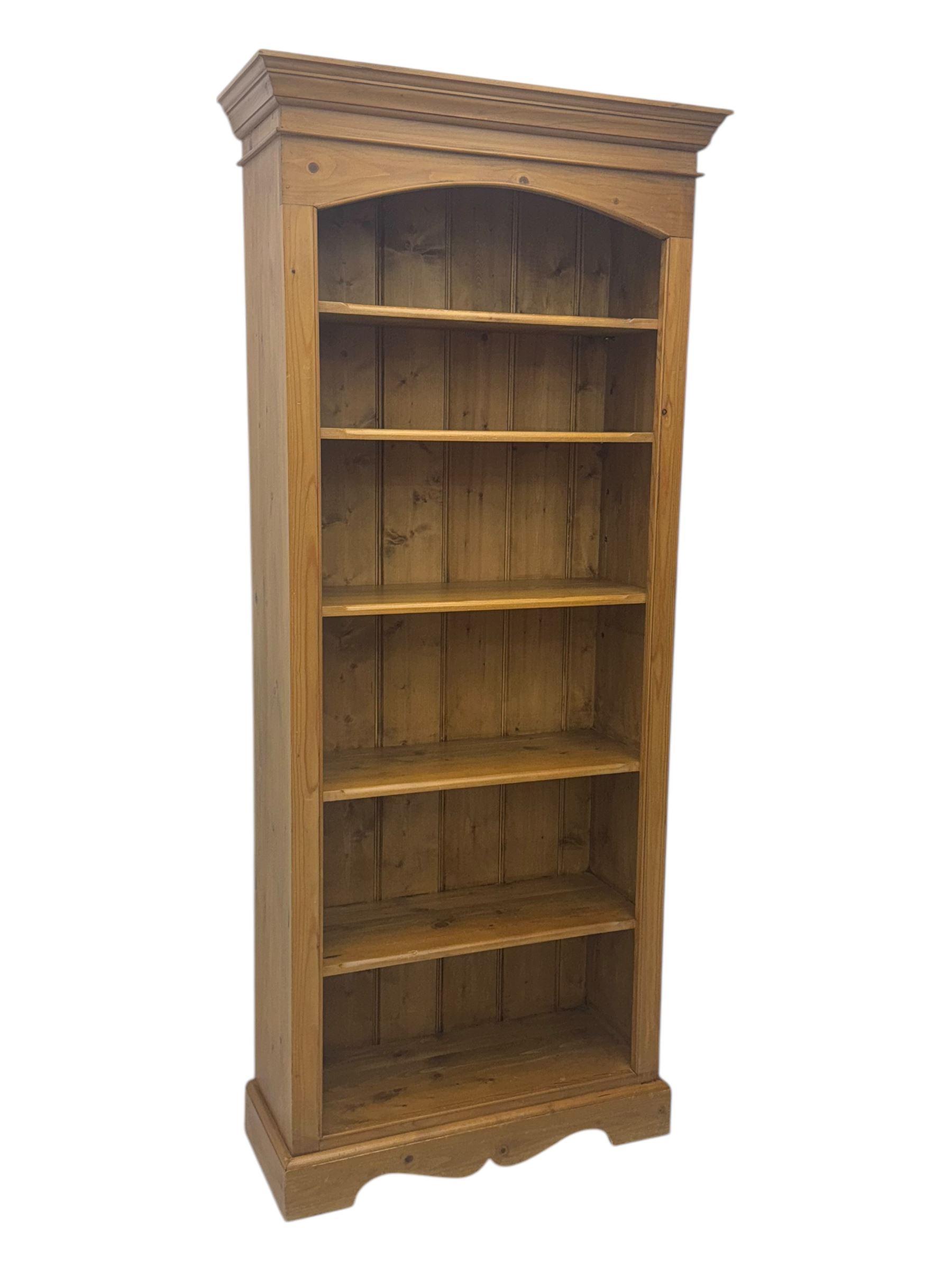 Early 20th century pine bookcase, projecting cornice over arched open shelving area with five adjustable shelves, on shaped plinth base
